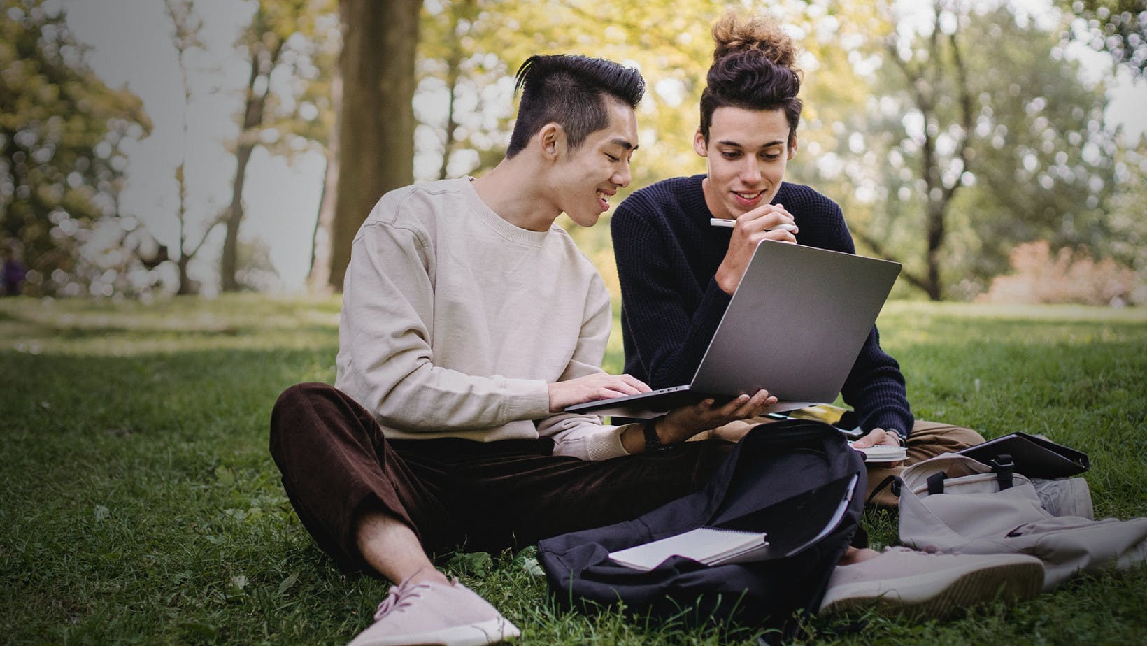 Two college students sitting on a lawn looking at a laptop
