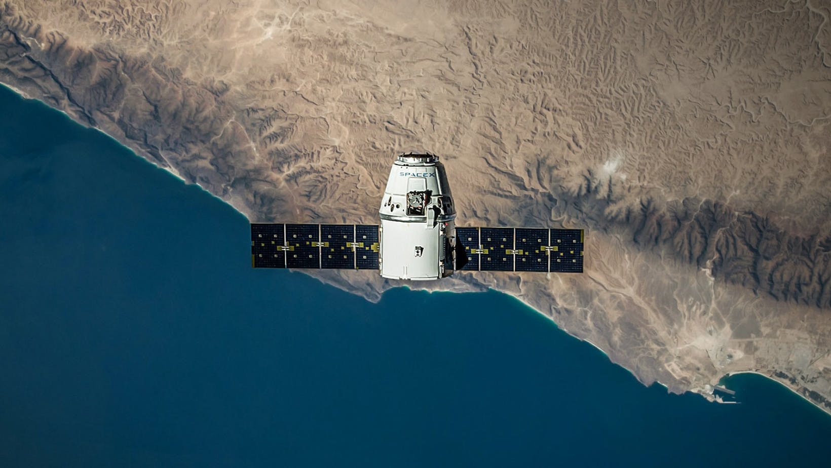 A spacecraft seen from above with coastline and water visible far in the distance beneath.