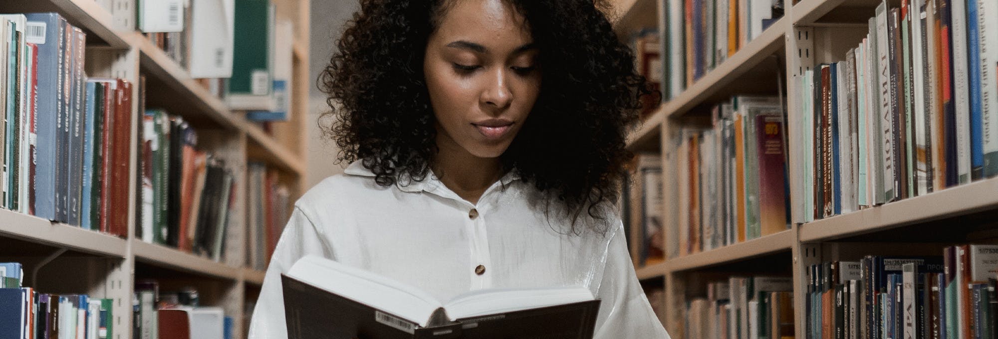 Black woman reading a literature book in a library aisle