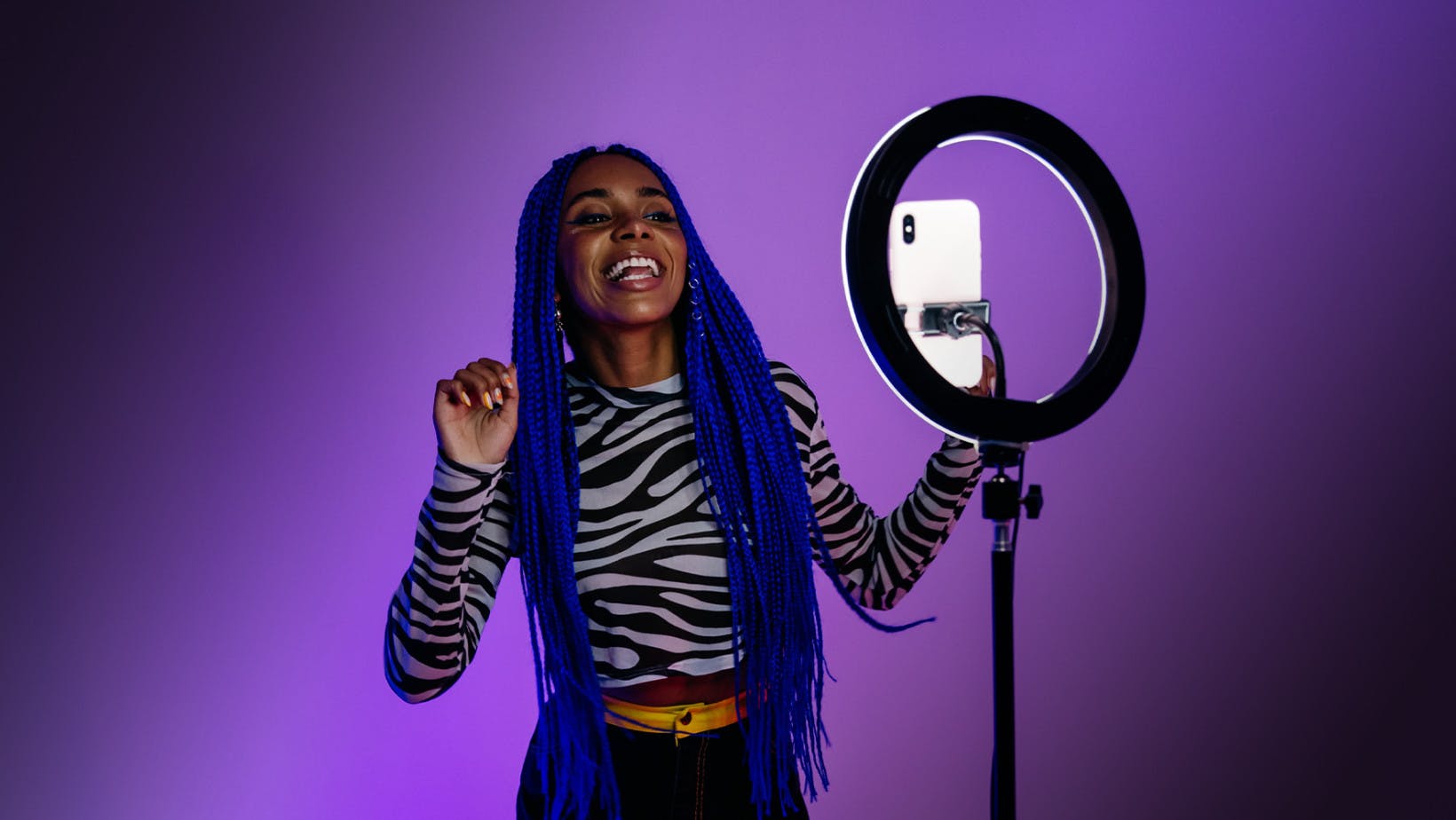 Woman with long blue hair recording herself on her phone with a ring light