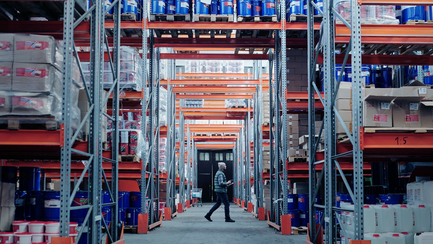 Rows of tall warehouse shelving with company products and a male worker walking through