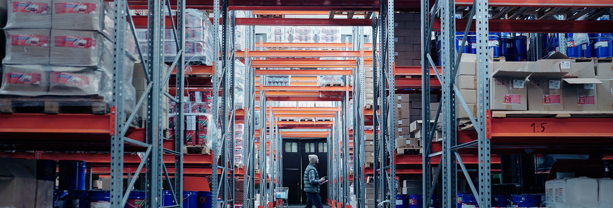 Rows of tall warehouse shelving with company products and a male worker walking through