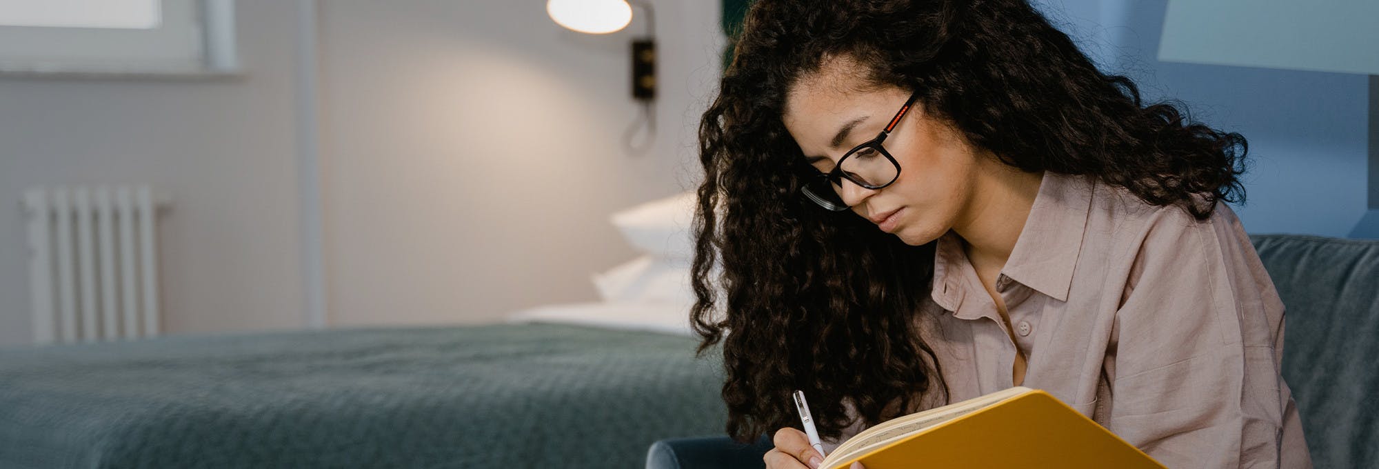 Woman with glasses on writing in a notebook reflecting on which college major to choose